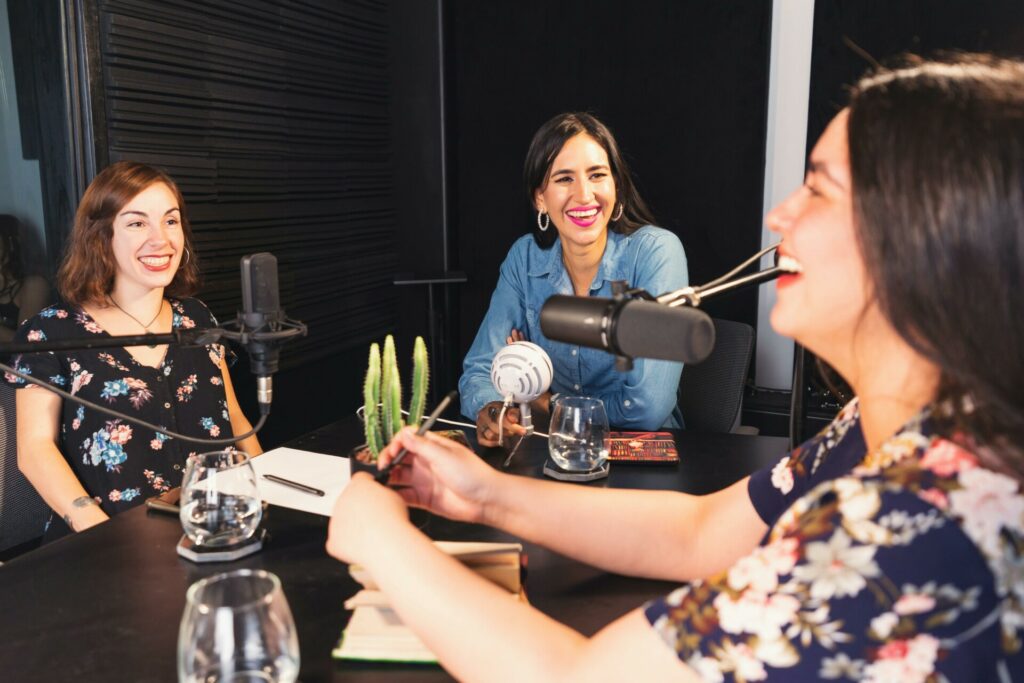 Trois femmes enregistrant un podcast en studio, échangeant autour de micros dans une ambiance détendue.