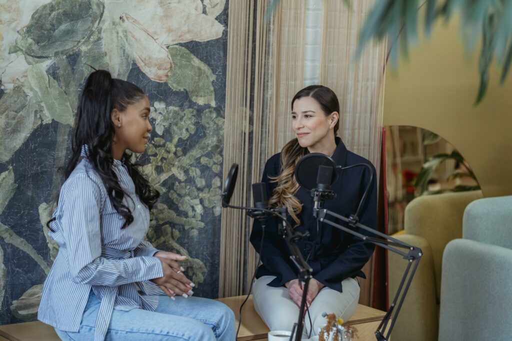 Deux femmes enregistrent une discussion audio dans un décor chaleureux, face à face avec des micros.